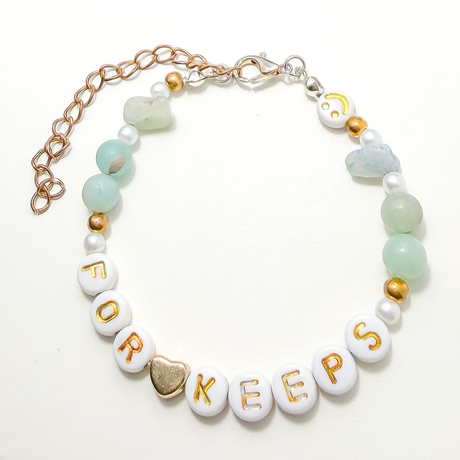 A mint and sea green bracelet with pearls, a gold heart, and letters spelling FOR KEEPS, with a clasp and extender chain